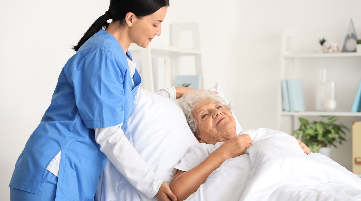 Infirmière en blouse blanche mesurant la tension artérielle d'une résidente âgée assise sur son lit dans une chambre lumineuse d'EHPAD, tensiomètre médical visible